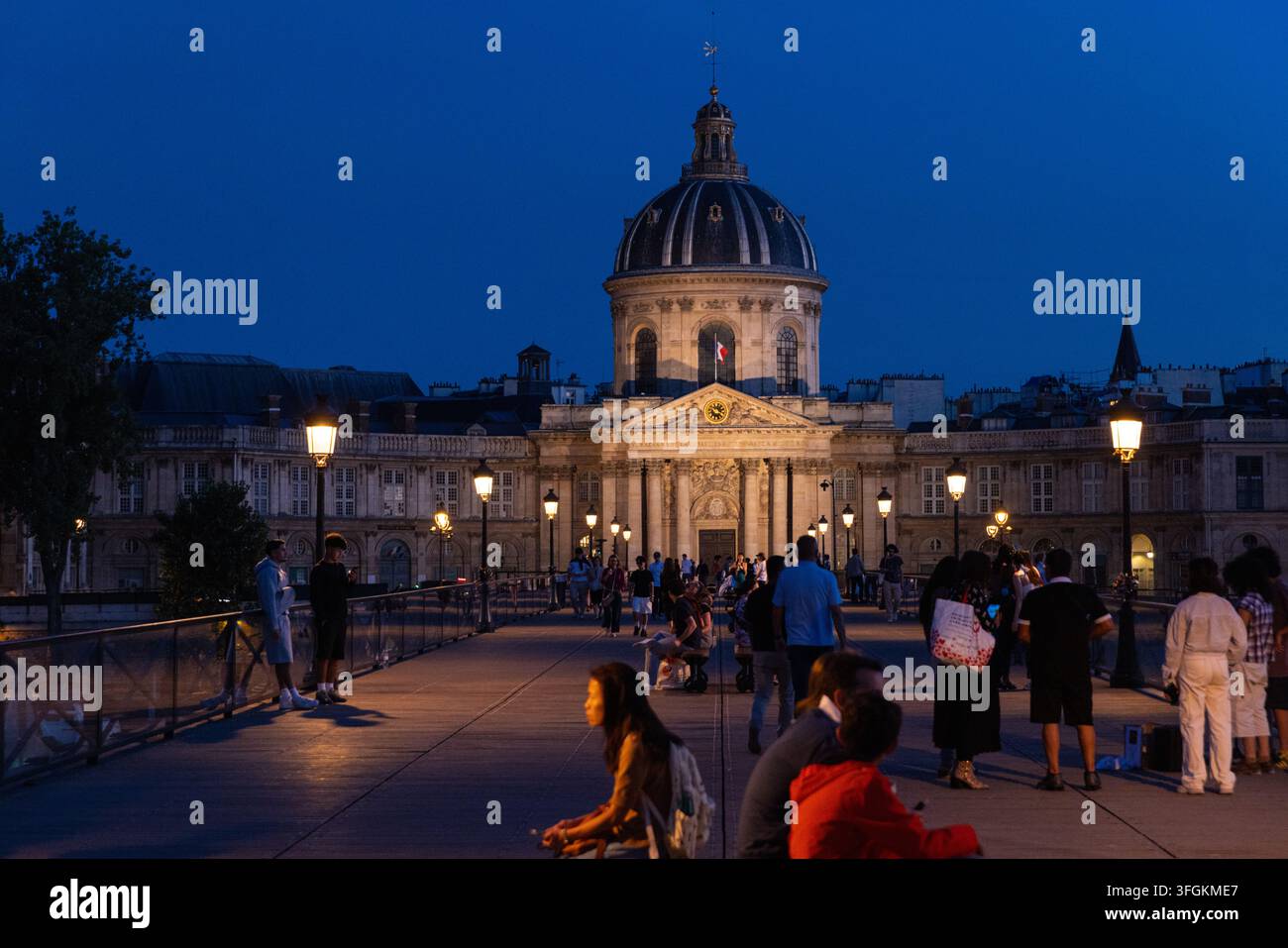 PARIS, FRANKREICH - 12. AUGUST 2026: Fußgänger versammeln sich und gehen bei Einbruch der Dunkelheit über die Fußgängerbrücke Pont des Arts Stockfoto