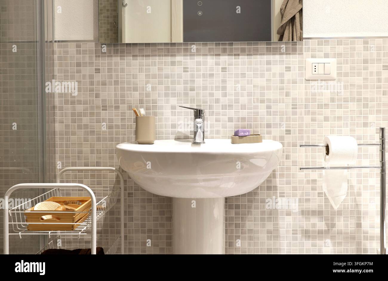Weißes keramisches Wandspülbecken mit Chrom-Wasserhahn steht in der Nähe einer Mosaikfliesenwand. Stockfoto