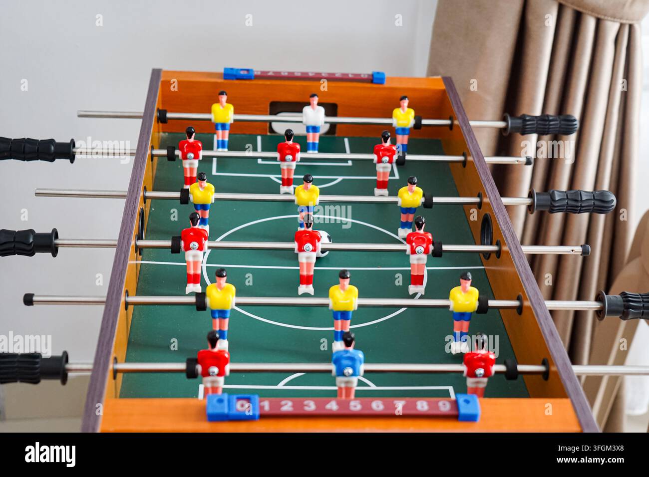 Eine Nahaufnahme eines Tischfußballspiels zeigt Miniaturfußballspieler in roten und gelben Trikots, die auf einem grünen Spielfeld angeordnet sind. Stockfoto