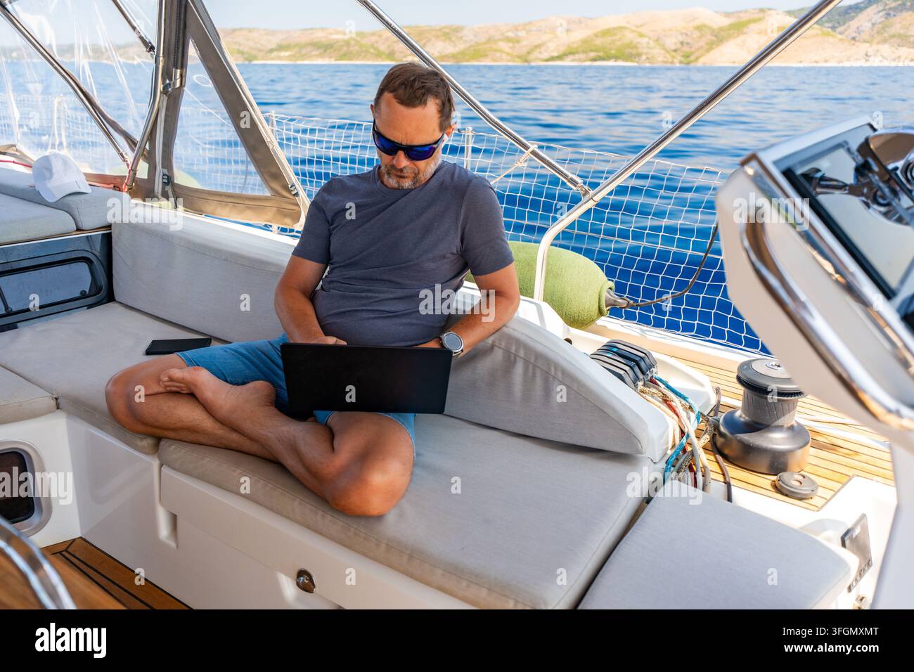 Konzentrierter Mann arbeitet an einem Laptop an Bord einer Segeljacht. Produktives Fernbüro in einer einzigartigen Reiseumgebung. Stockfoto