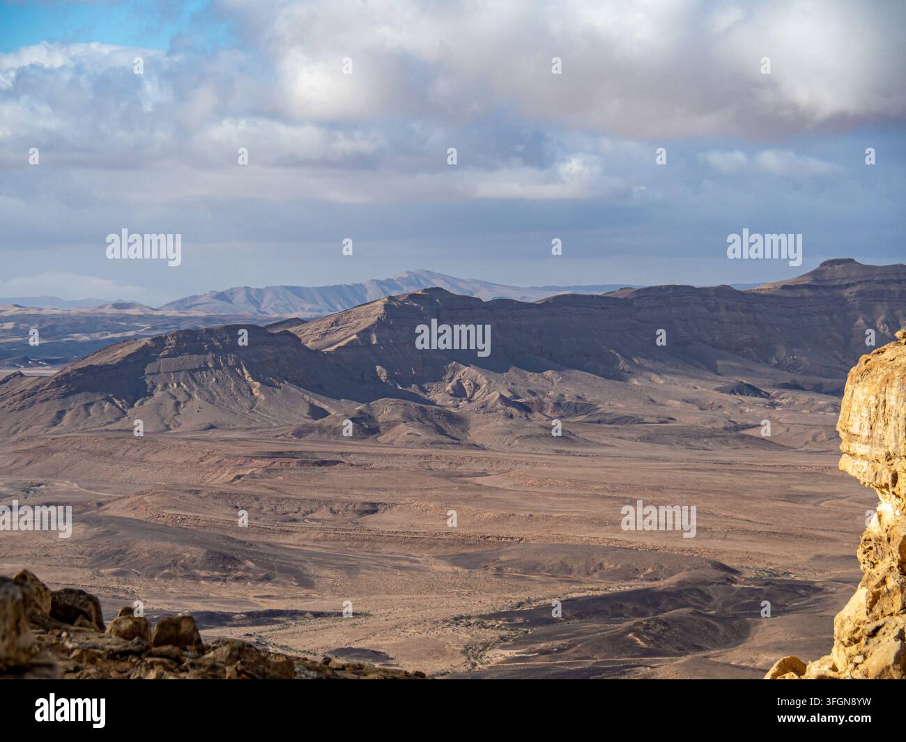 Sonnenbeschienene Sedimentkämme und Schluchtwände erstrecken sich bis zu einem dunstigen Horizont unter einem Himmel voller dramatischer Kumuluswolken über einem weiten Wüstenkrater Stockfoto