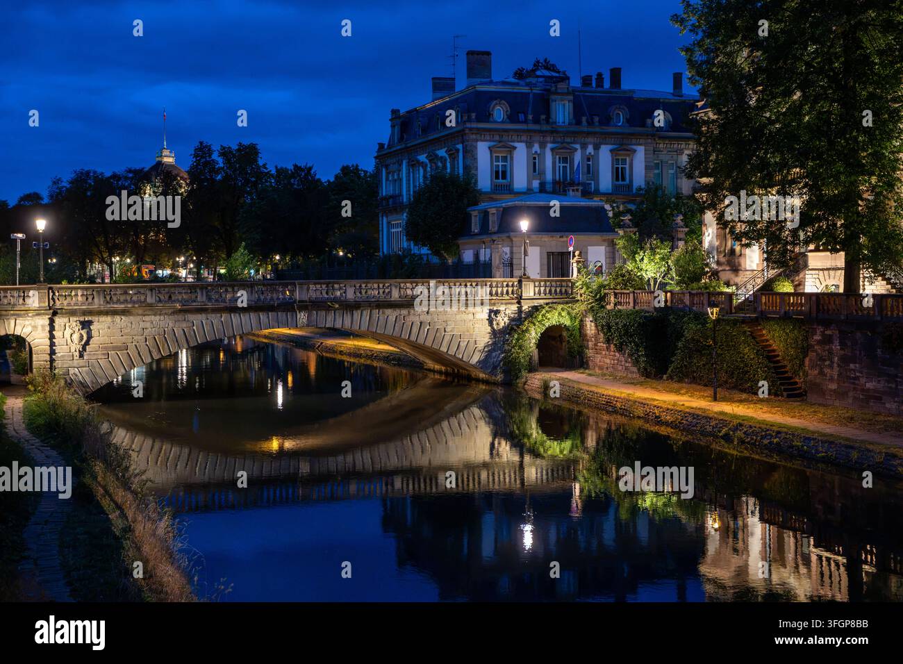 Ansicht des beleuchteten Steinbogens Pont du Corbeau, der sich im Ill-Fluss während der Blauen Stunde in Strasbourg, Bas-Rhin, Elsaß, Frankreich spiegelt Stockfoto