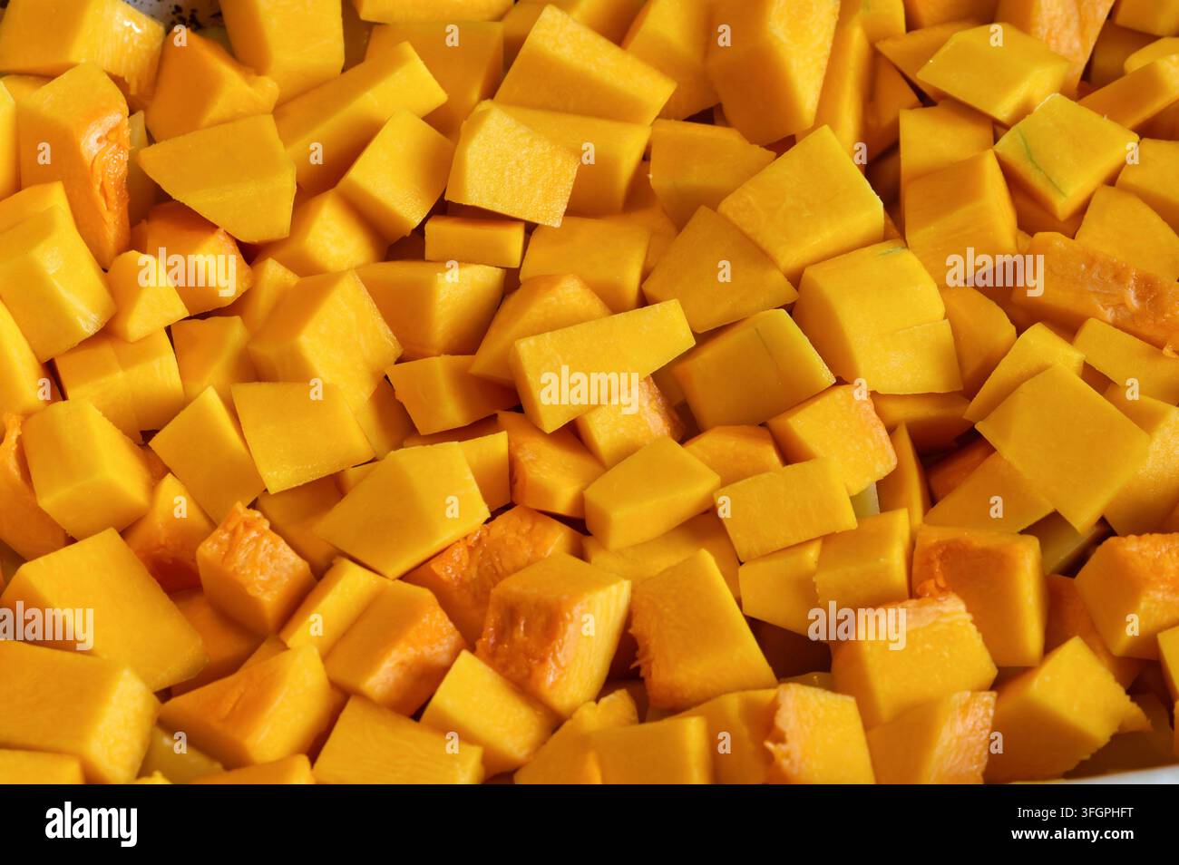 Vollbild-Nahaufnahme von gehackten orangefarbenen Kürbiswürfeln, bereit zum Kochen. Frisches Herbstgemüse-Hintergrundkonzept Stockfoto