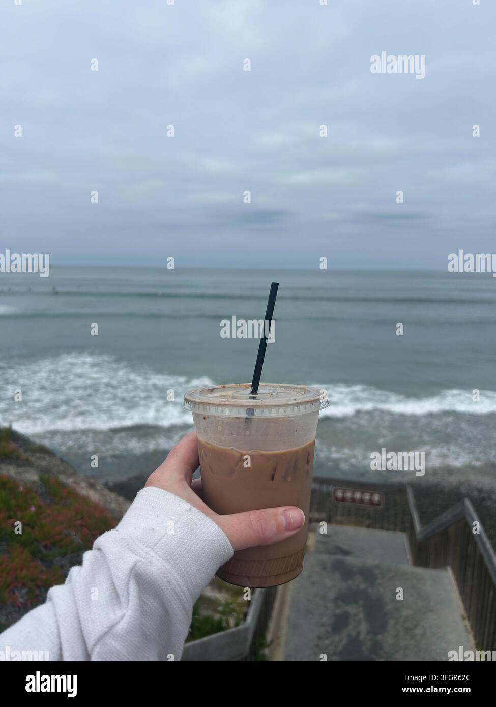 Hält einen Eiskaffee mit Blick auf den Ozean Stockfoto