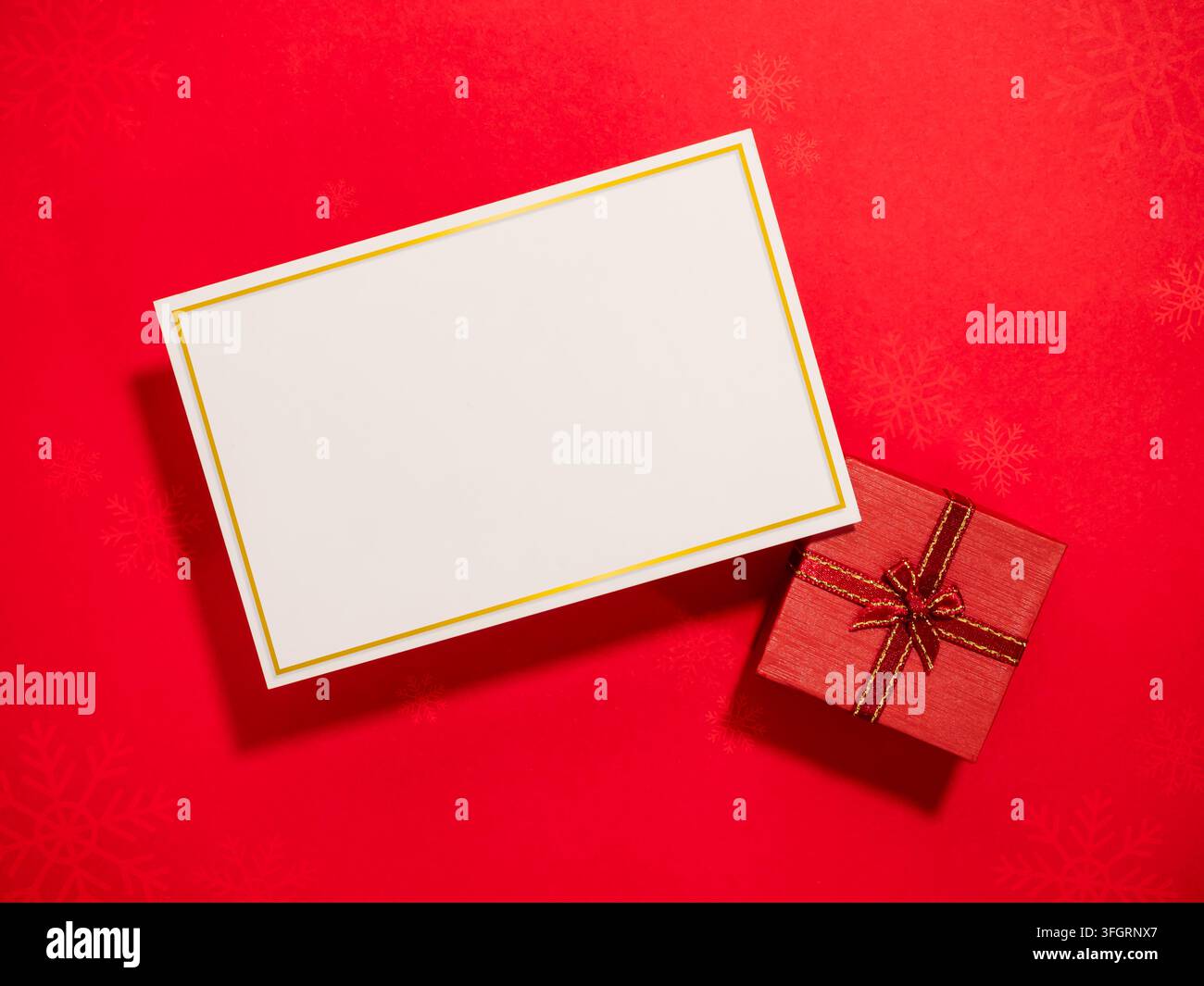 Elegante Feiertagsgrußkartenvorlage mit leerem weißem Nachrichtenkarten und roter Geschenkschachtel auf festlichem Weihnachts Hintergrund. Unternehmensgrüße, saisonales Probedruck Stockfoto