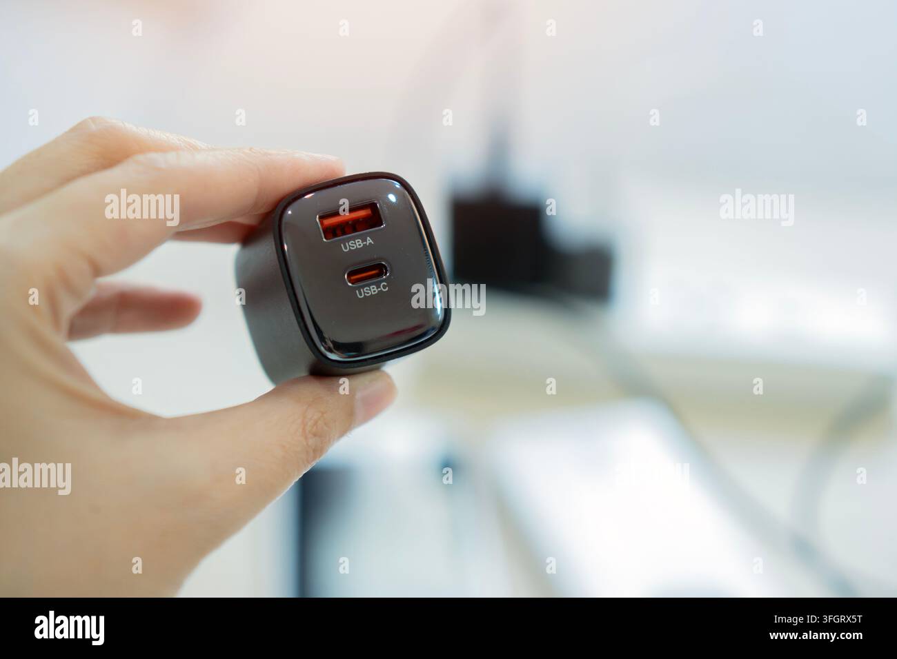 Hand, die einen kleinen schwarzen kompakten Dual-Port-USB-Netzadapter hält, der Typ-C- und Typ-A-Ladeanschlüsse zeigt. Selektive Fokussierung. Stockfoto