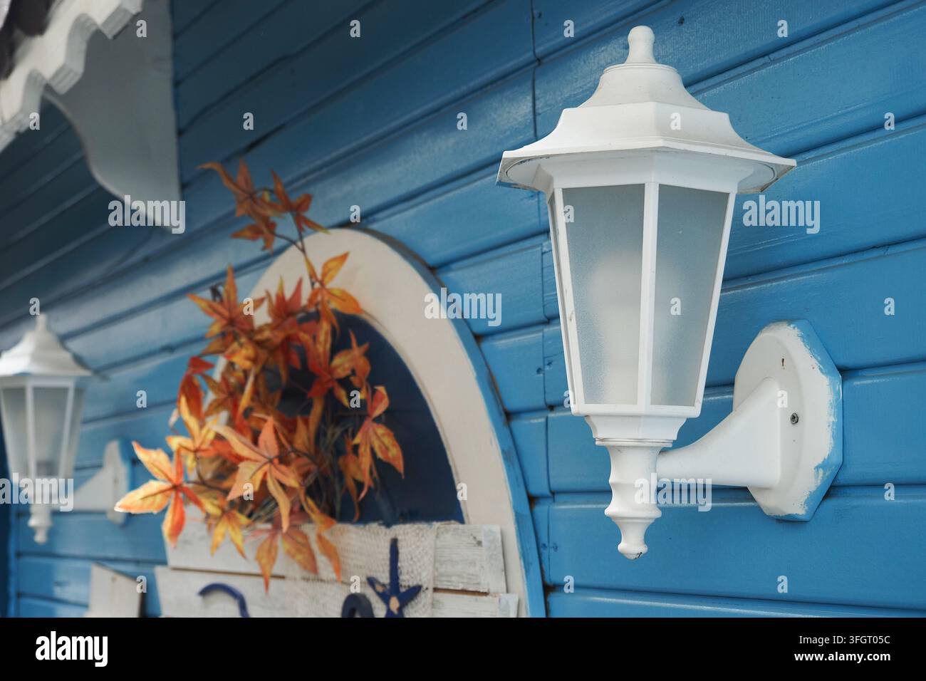 Lichtleuchte und Wanddekoration an einem blauen Holzgebäude mit Herbstblättern Stockfoto
