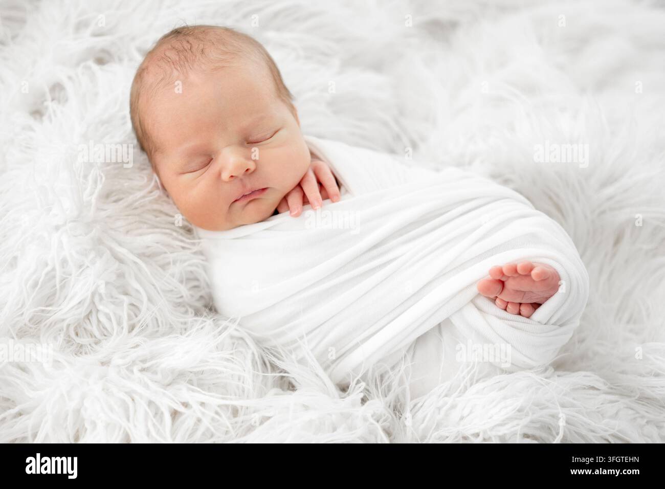 Friedliches Baby, das tagsüber bequem auf einem flauschigen weißen Teppich ruht Stockfoto