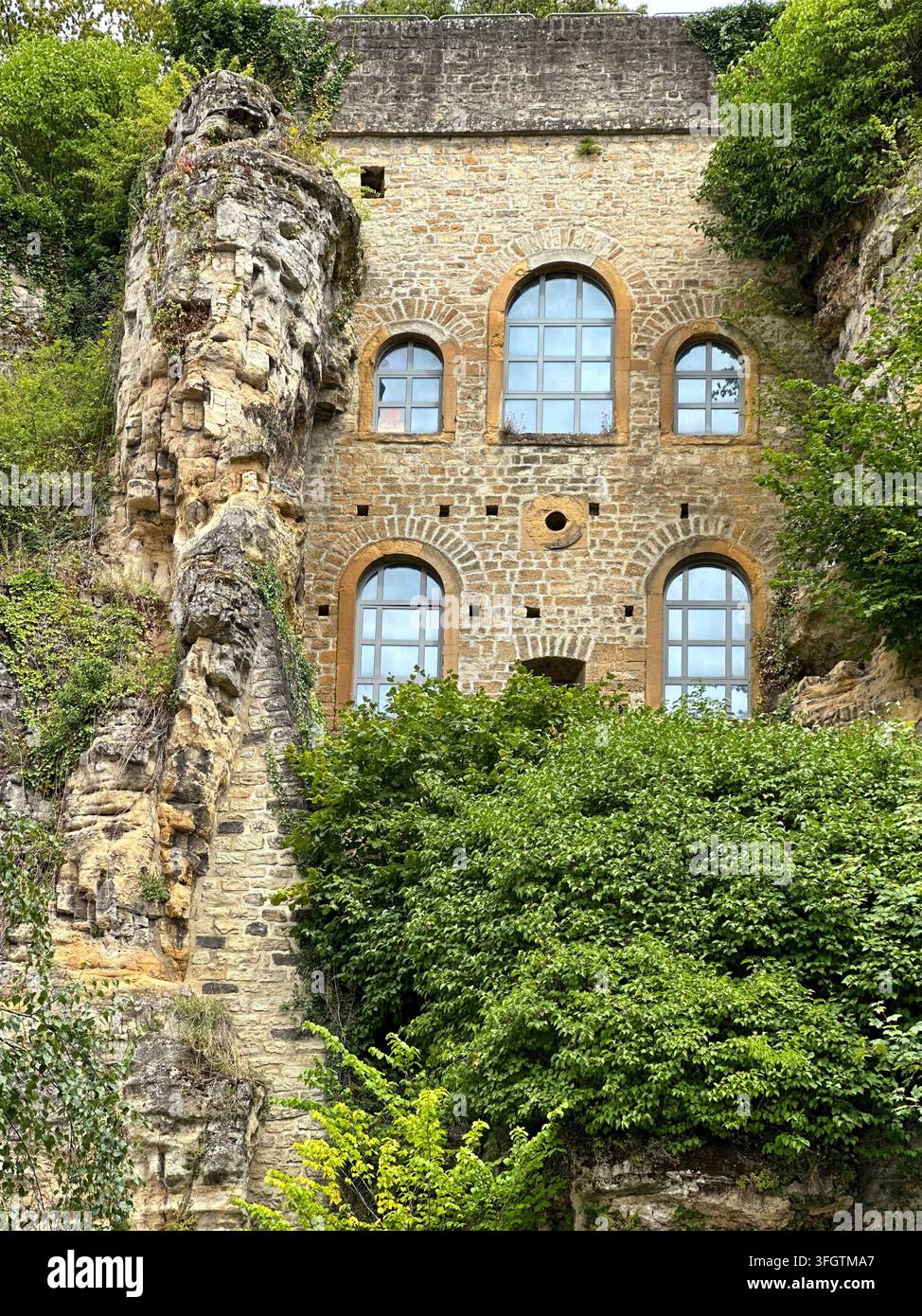 Historische Steinfassaden, die in eine Felswand eingebettet ist, mit gewölbten Gitterfenstern. Antike Steinarchitektur, die in eine schroffe Felswand eingebaut ist und - Smartphone-aufgenommenes Stockfoto