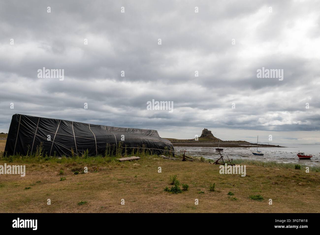 Ein altes Fischerboot, das auf dem Kopf liegend als Bootslagerhütte am Strand von Lindisfarne Holy Island genutzt wird, mit Lindisfarne Castle im Hintergrund Stockfoto