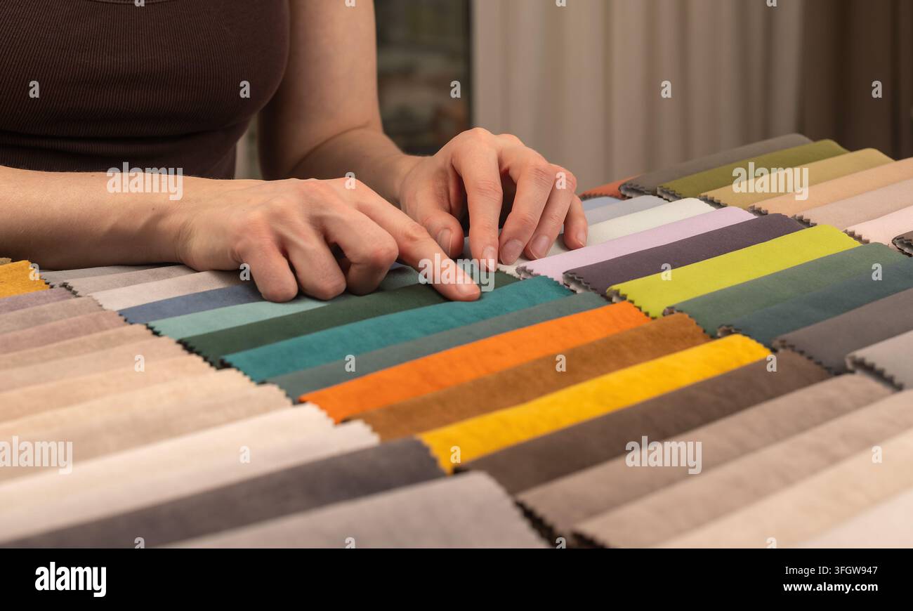 Hände wählen Stoffmuster aus einer Polsterauswahl. Bunte Textilstreifen bedecken die Oberfläche. Stockfoto