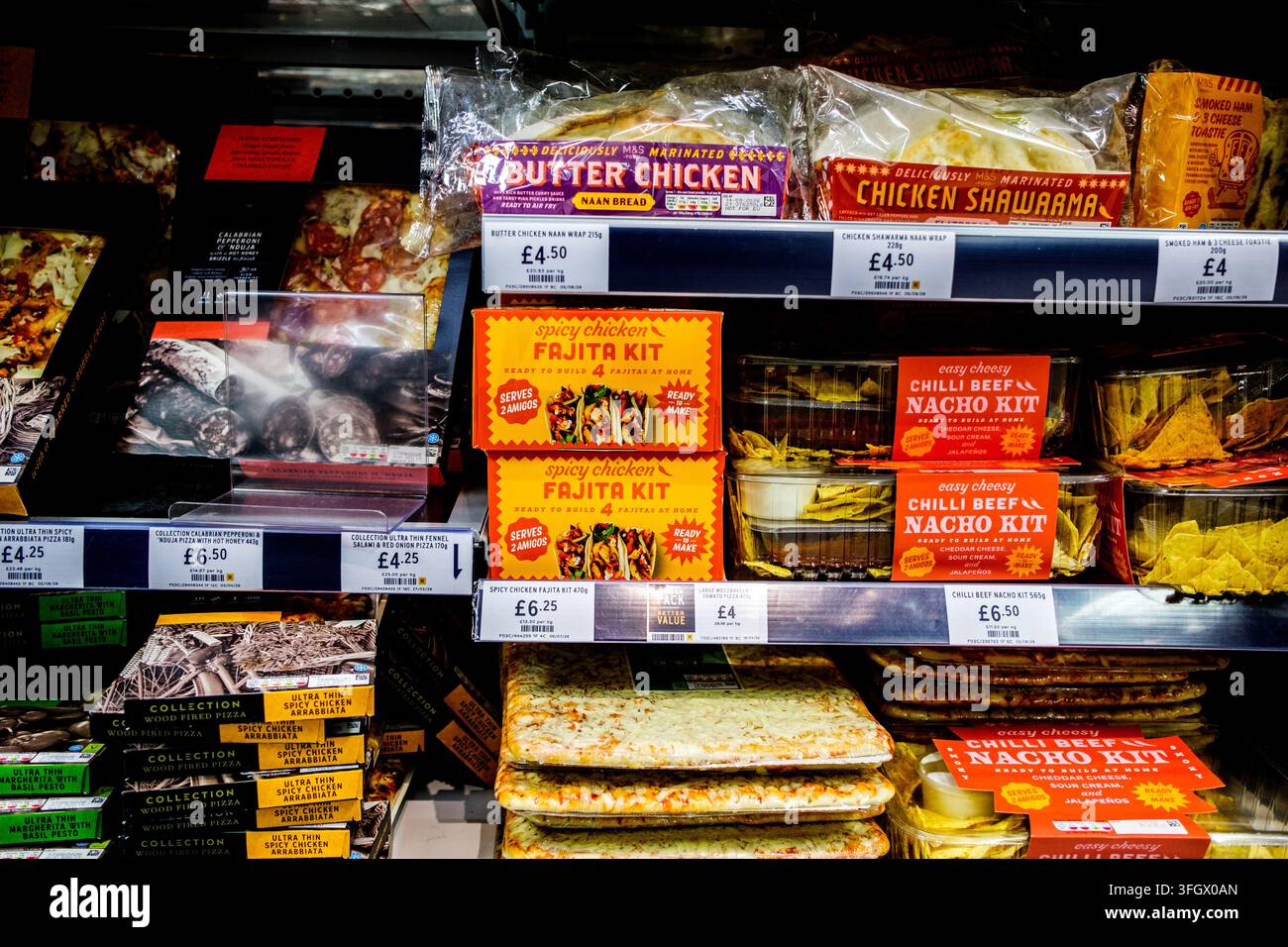 London, UK, 12. September 2026, Kühlregal im Supermarkt mit Marks And Spencer-Pizzas, indischen Wraps und mexikanischen Mahlzeit-Kits mit Preisschild Stockfoto