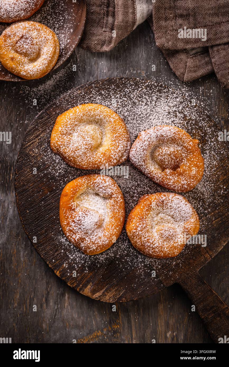 Goldbraun gebratene Gebäckstücke mit Puderzucker bestreut auf einem rustikalen Holzbrett Stockfoto