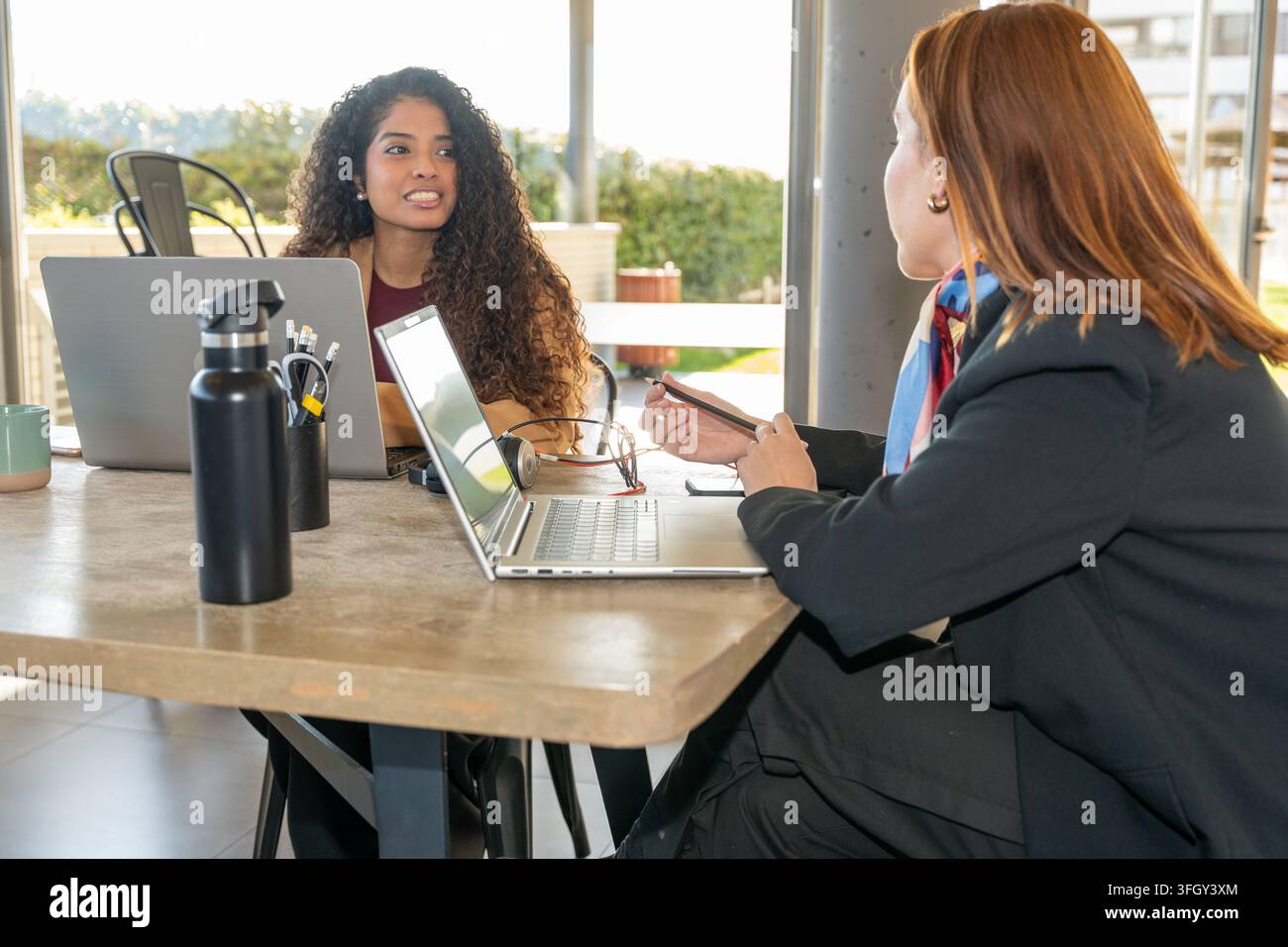 Zwei Geschäftsfrauen, die zusammen an Laptops in einem modernen Büro diskutieren und arbeiten Stockfoto