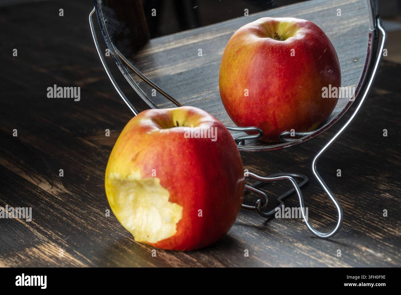 Der gebissene Apfel spiegelt sich im Spiegel, Nahaufnahme. Betrugskonzept Stockfoto