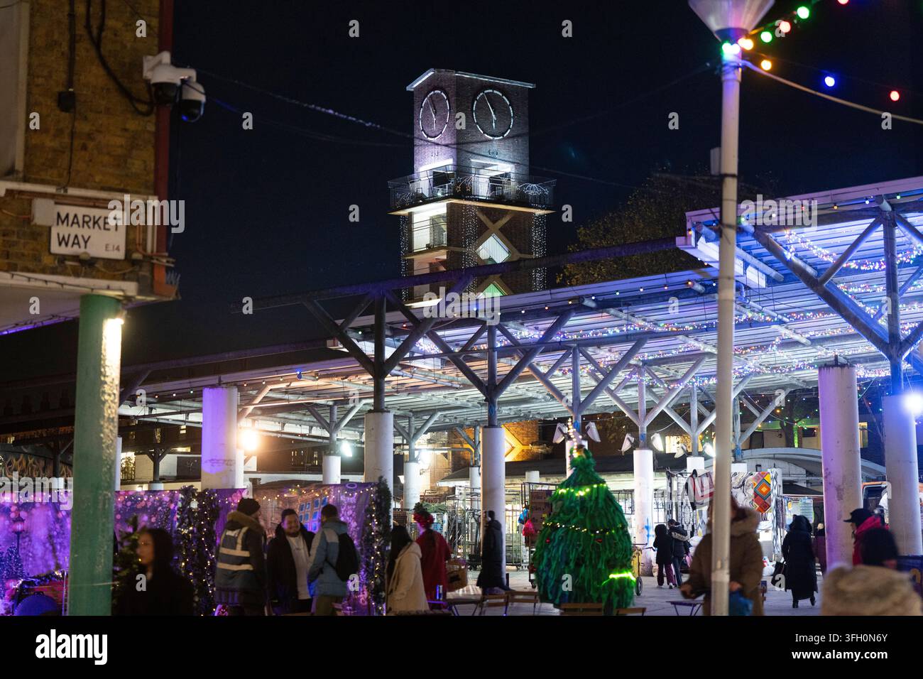 Einkäufer versammeln sich unter festlichen Lichtern am Chrisp Street Market in Poplar, London, in der Nähe des ikonischen Uhrturms am Market Way. Stockfoto
