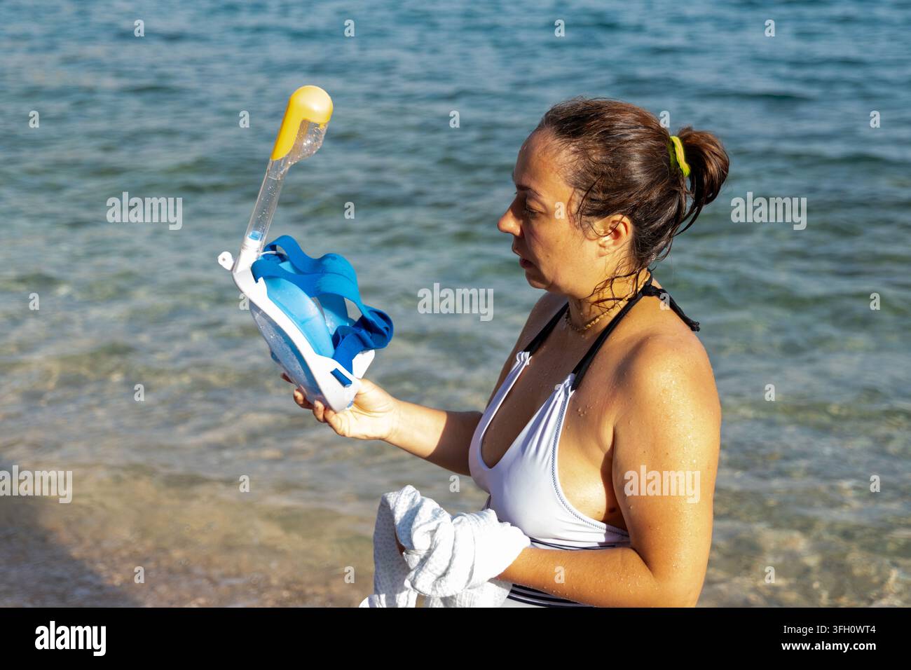 Frau steht am Ufer und hält eine Vollgesichts-Schnorchelmaske an einem sonnigen Strand. Stockfoto