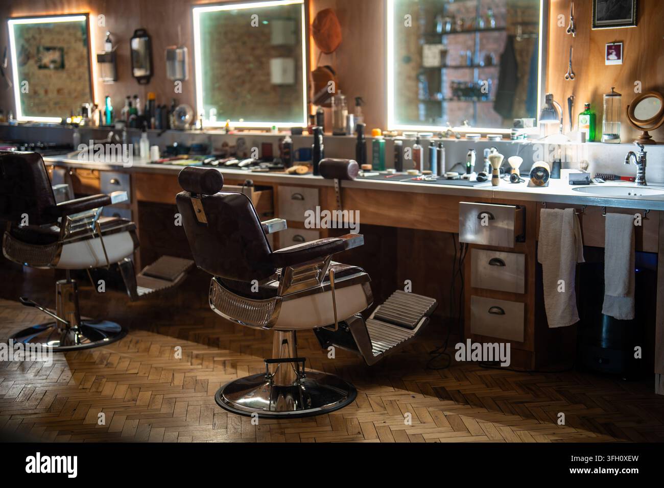 Gemütliches Interieur eines Friseursalons mit klassischen Vintage-Stühlen, beleuchteten Spiegeln und professionellen Werkzeugen. Stockfoto