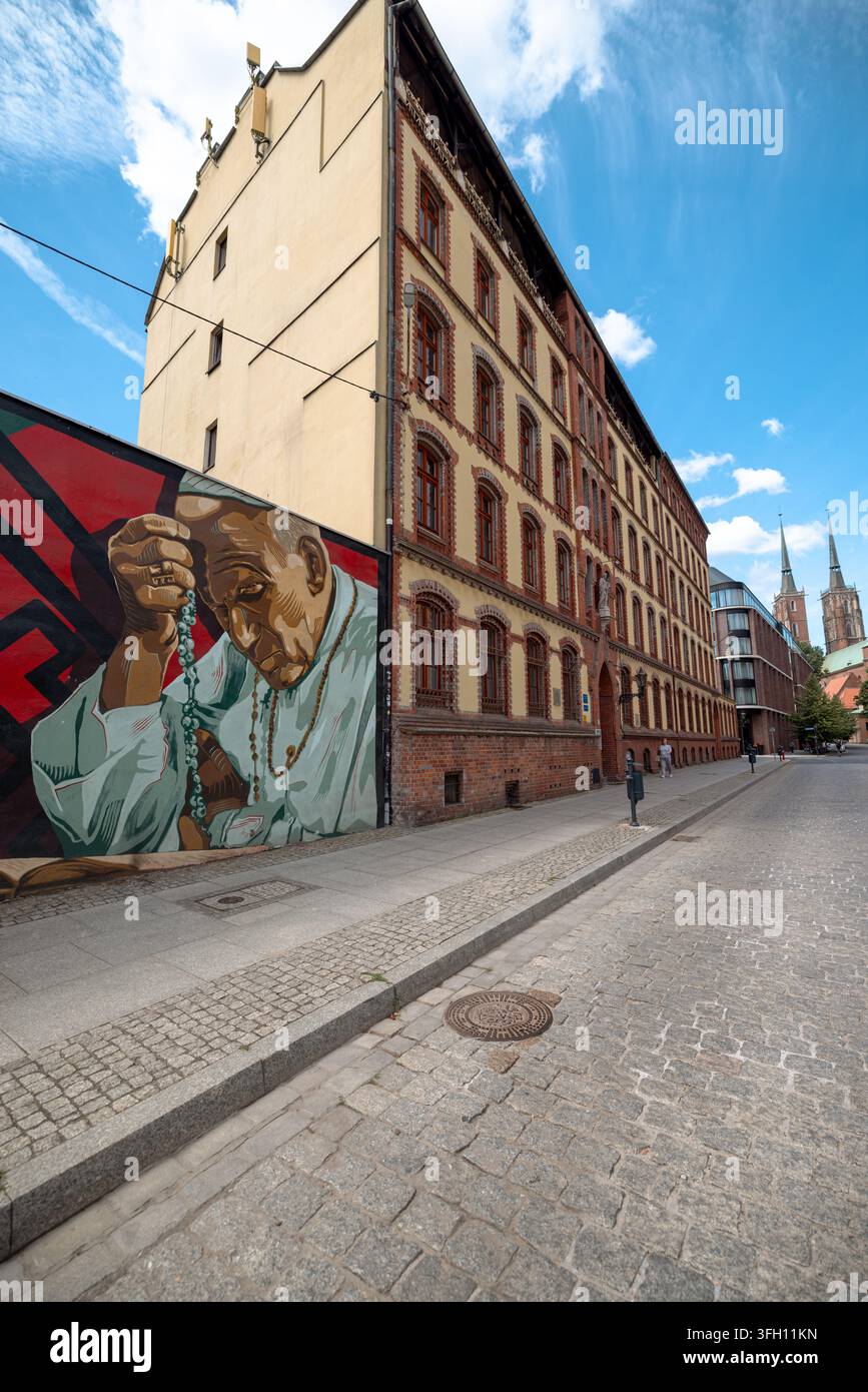 Ein zeitgenössisches Porträt-Wandgemälde bedeckt eine lange Wand neben einem historischen Backsteingebäude in der Nähe von Ostrow Tumski. Stockfoto