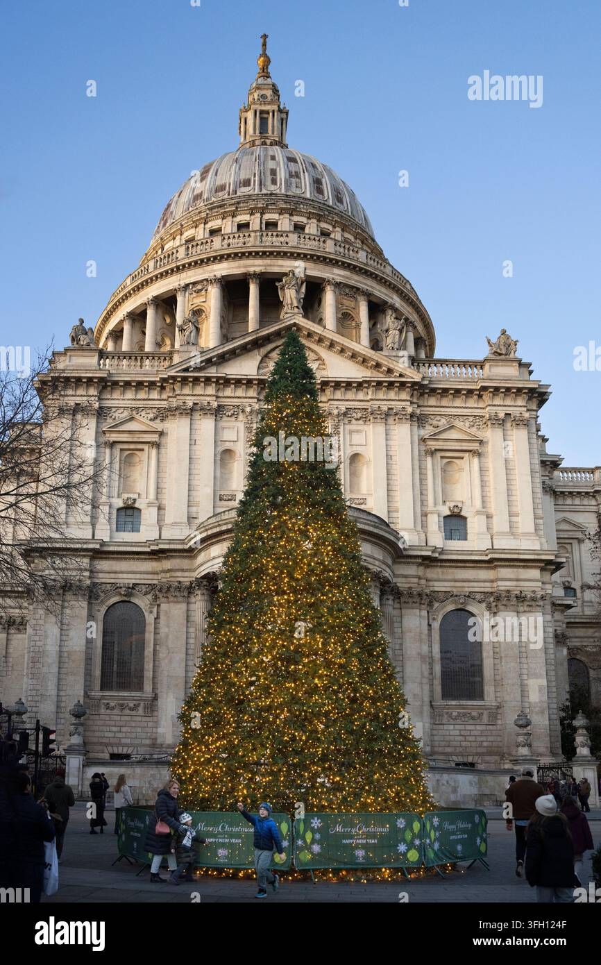 Besucher feiern die Feiertage in der Nähe eines beleuchteten Weihnachtsbaums vor der St. Paul's Cathedral in der City of London, England. Stockfoto