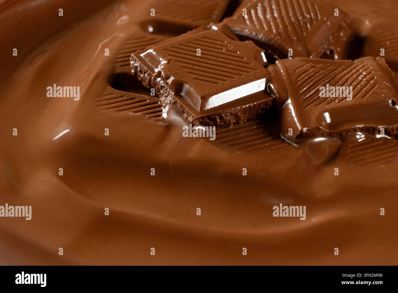 Schokoladenstücke, die zu glatter, warmer Schokoladenflüssigkeit schmelzen, Makroaufnahme. Stockfoto
