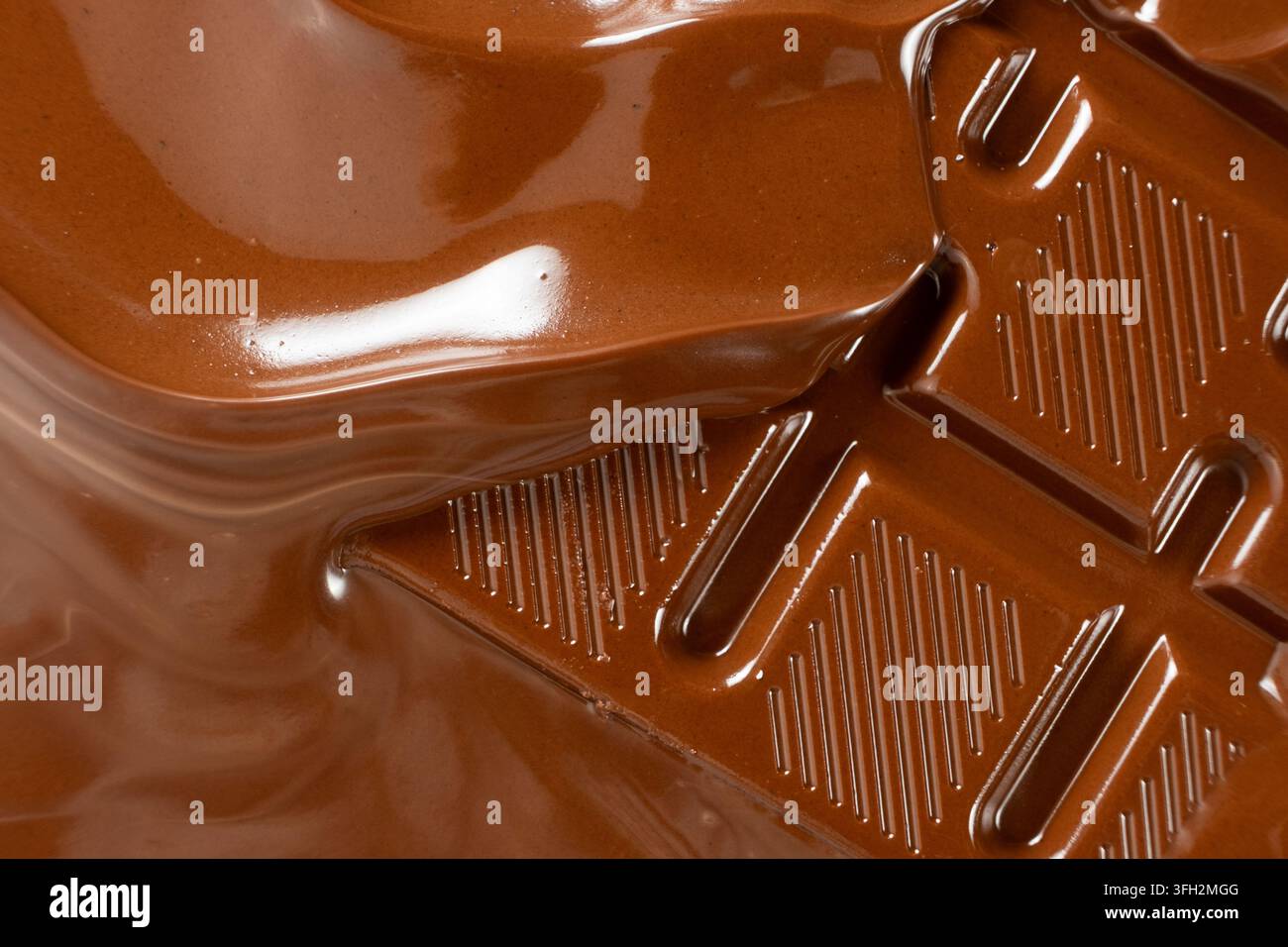 Warme flüssige Schokolade, die über einen festen Milchschokoladenriegel fließt, Makroaufnahme. Stockfoto