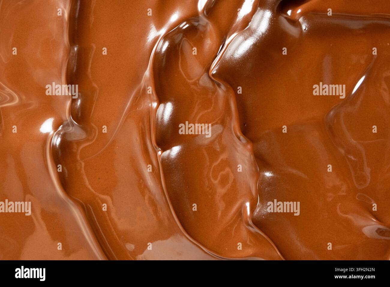 Wirbelnder geschmolzener Milchschokoladenhintergrund mit glänzender Wellenstruktur. Stockfoto