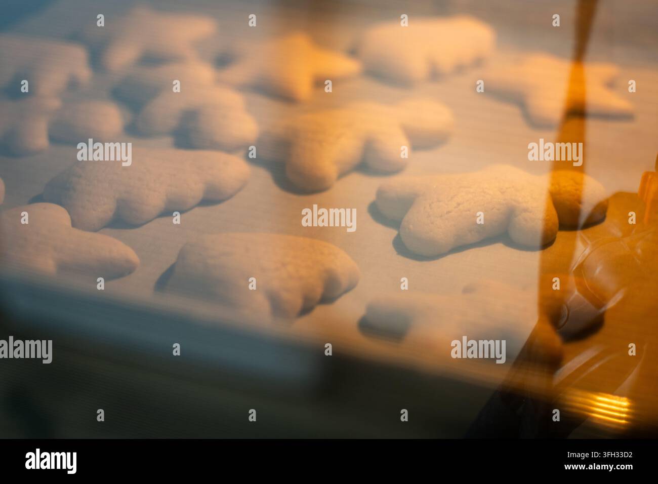 Weihnachtsplätzchen in festlichen Formen backen auf einem Blech in einem warmen Ofen, gesehen durch die Ofentür. Stockfoto