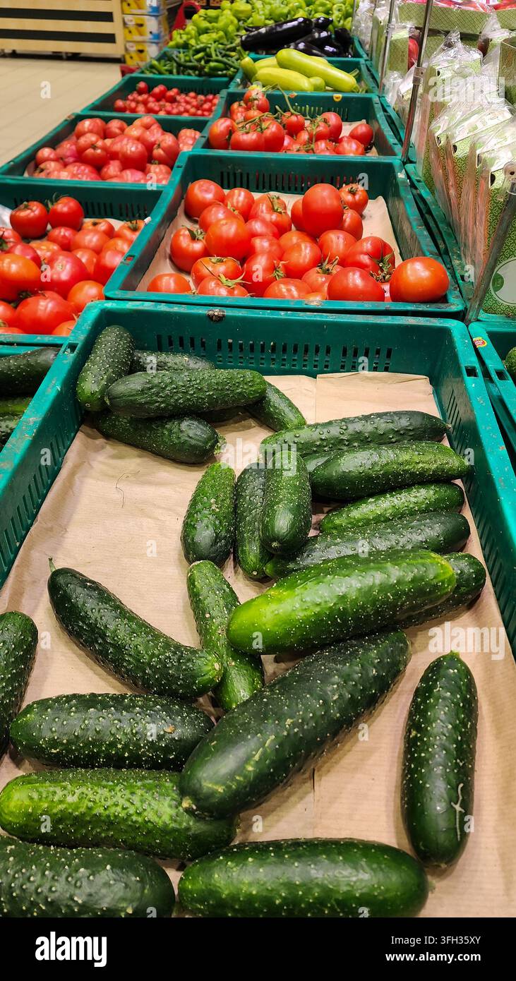 Gurken, Tomaten und verschiedene frische Gemüsesorten sind in Kisten im Obst- und Gemüsegang eines Supermarkts reichlich vorhanden und bieten gesunde Optionen für den Lebensmitteleinkauf Stockfoto