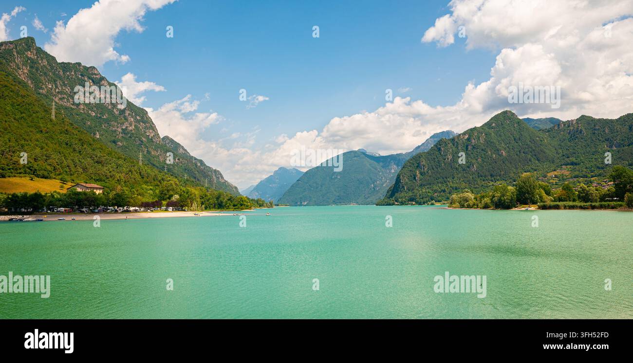 Weitläufiger Blick auf den smaragdgrünen Alpensee Idro, Italien, zwischen grünen Bergen unter blauem Sommerhimmel mit Wolkenpartie. Stockfoto