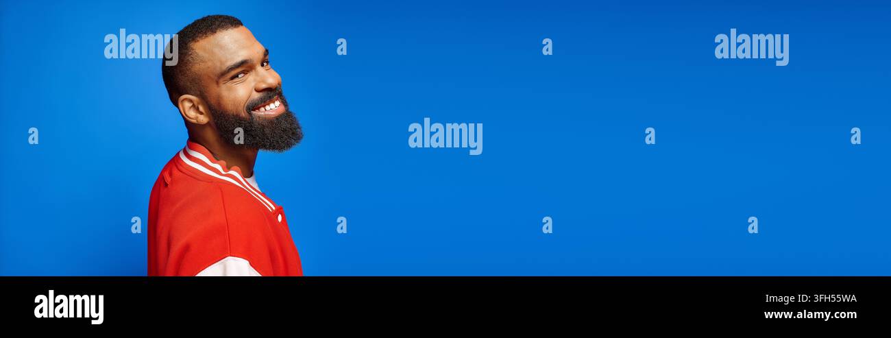 Ein gutaussehender junger afroamerikanischer Mann in stilvoller Kleidung teilt ein fröhliches Lächeln in einer kühnen Umgebung. Stockfoto