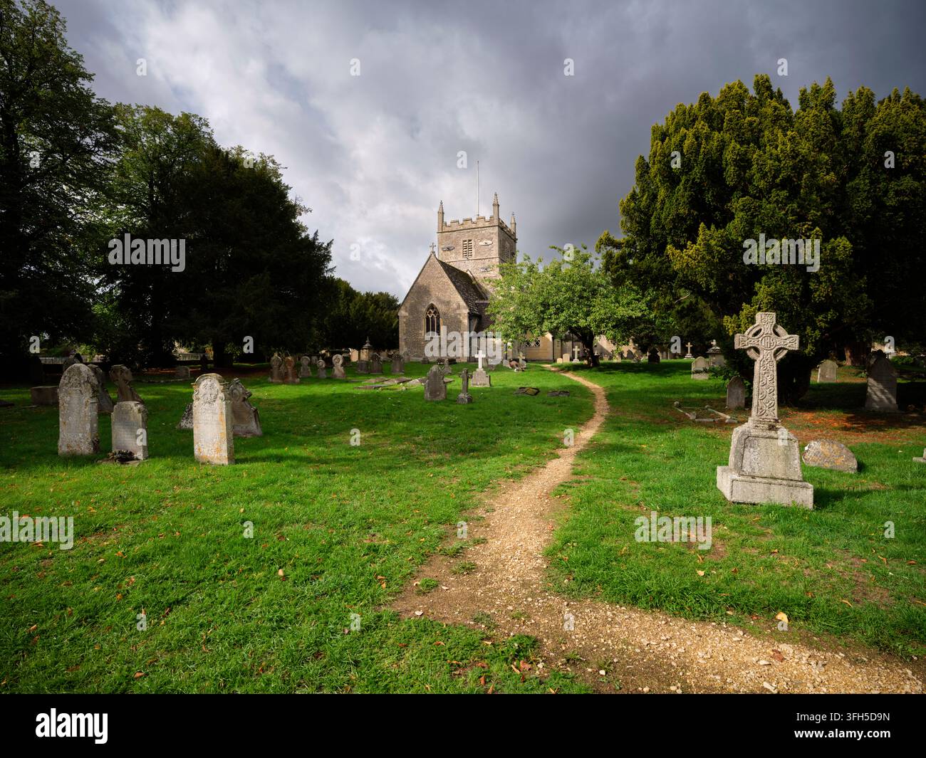 All Hallows Kirche und historischer Friedhof mit Steinkreuz und Weg im Cotswold-Dorf South Cerney, Gloucestershire, UK. Stockfoto