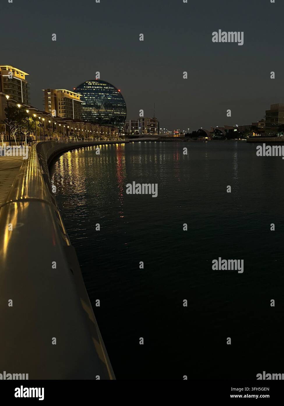 Wasserfront von Abu Dhabi bei Nacht mit beleuchteten modernen Gebäuden und Spiegelungen auf dem Wasser in den Vereinigten Arabischen Emiraten - Smartphone-aufgenommenes Stockfoto