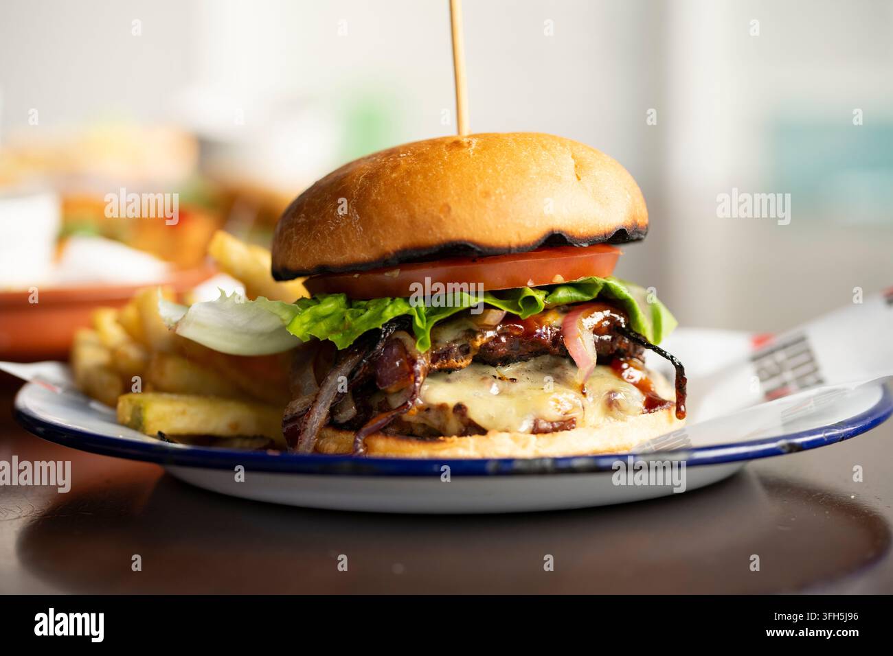 Saftiger Burger serviert mit knusprigen Pommes in einer lebhaften Essensumgebung Stockfoto