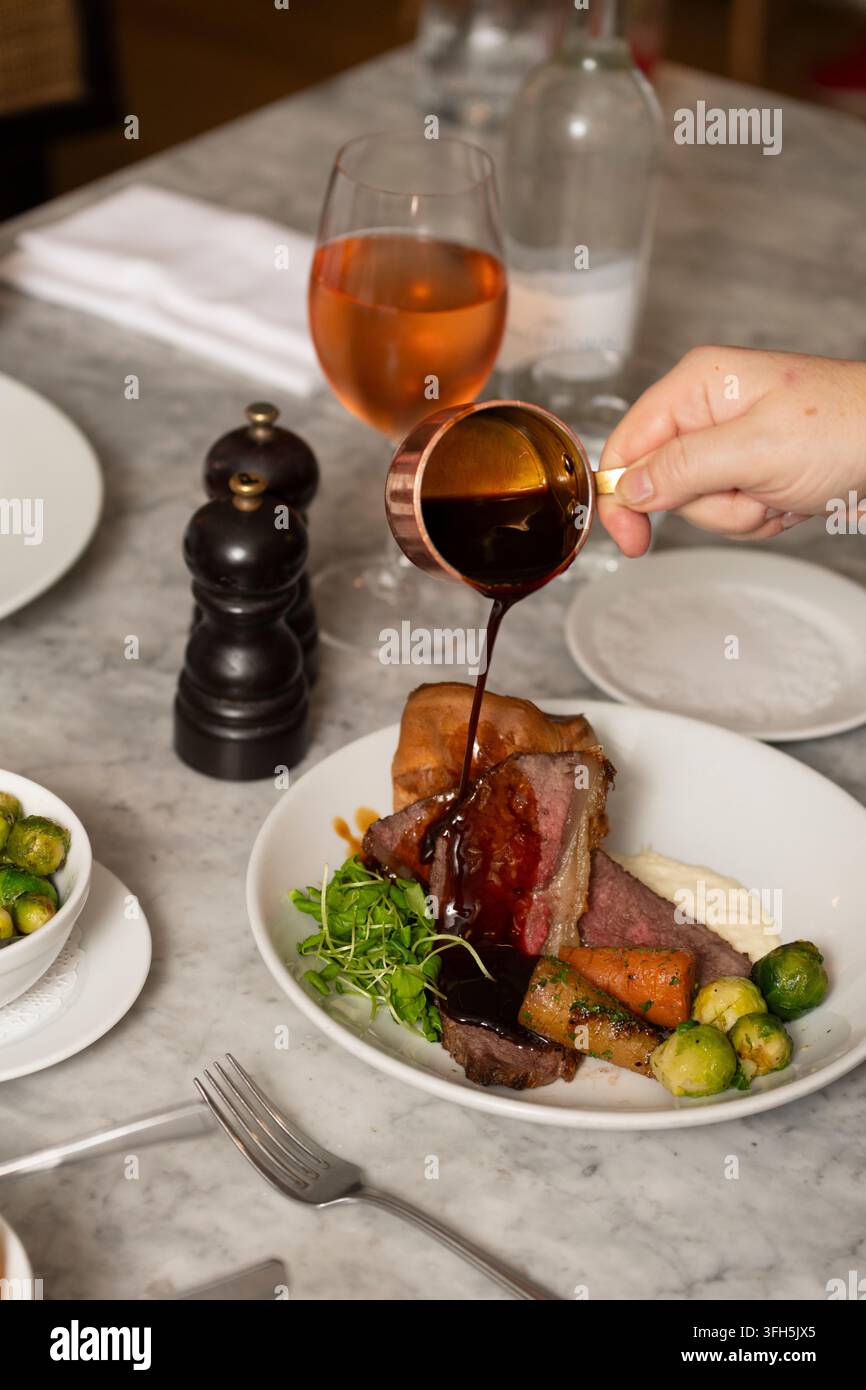 Köstliches Roast Beef serviert mit Gemüse und reichhaltiger Soße in einer gemütlichen Essensumgebung Stockfoto