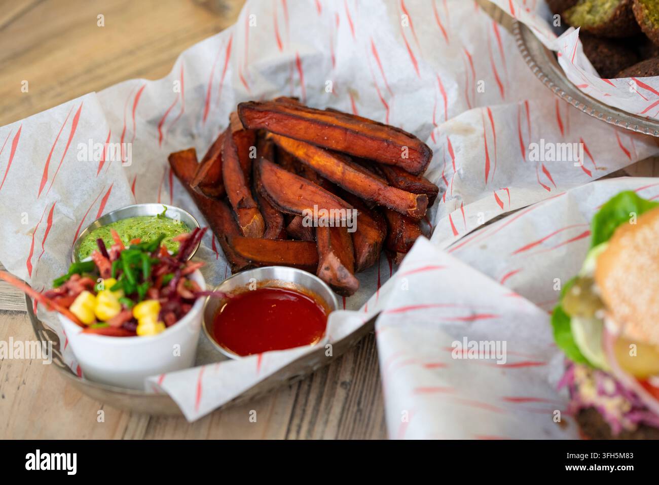 Knusprige Süßkartoffel Pommes, serviert mit einzigartigen Dipsaucen in einer gemütlichen Essensumgebung Stockfoto