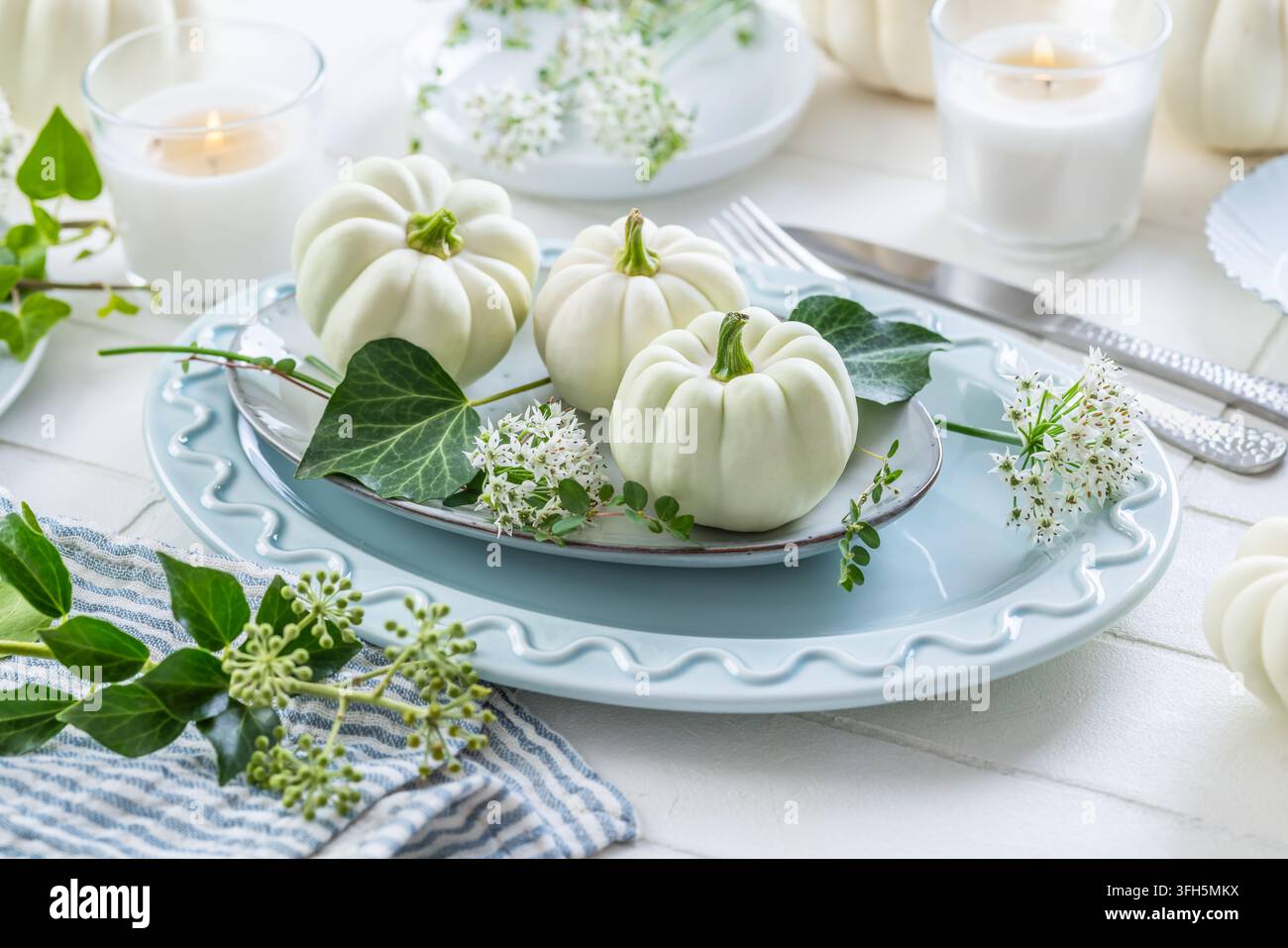 Elegante Herbsttischdekoration mit weißen Kürbissen und zartem Grün Stockfoto