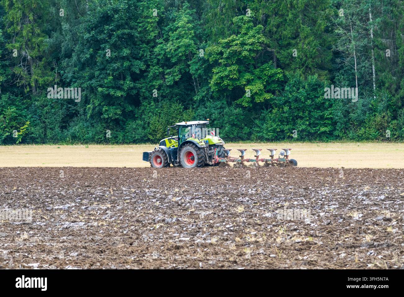 KOCĒNI, LETTLAND - 28. AUGUST 2026: CLAAS-Traktor zieht einen Mehrfurchempflug, während er ein Agrarfeld bei Kocēni bestellt. Stockfoto
