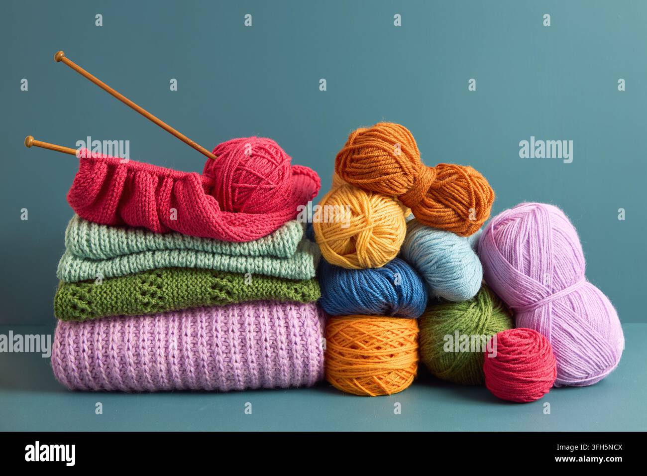 Farbenfrohe Wollknäuel und handgemachte Strickwaren, die auf einem Tisch arrangiert sind, präsentieren Stricken, Textilkunst, Kreativität und handgefertigte Faserkunst. Stockfoto