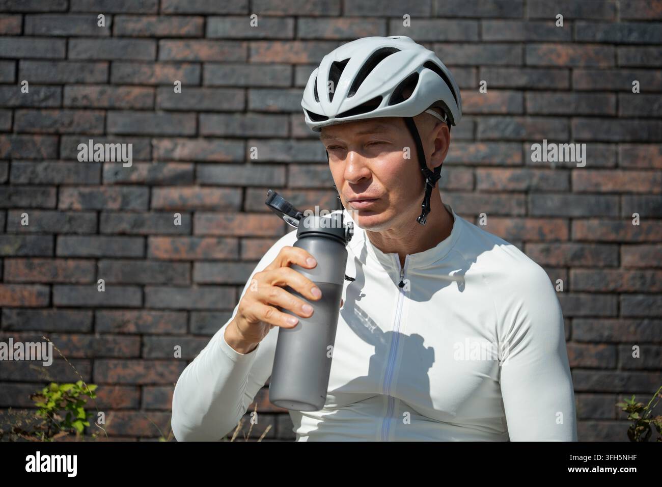 Ermüdeter männlicher Radfahrer macht eine Pause mit Wasserflasche nach einer Langstreckenfahrt. Konzept der Erholung, des Umgangs mit körperlicher Belastung, der Ausdauer und der Gesundheit du Stockfoto