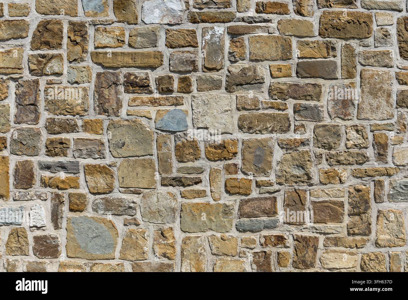 Nahaufnahme, vollflächige Textur einer traditionellen Steinmauer, gebaut aus unregelmäßig geformten Natursteinblöcken in verschiedenen erdigen Tönen Stockfoto