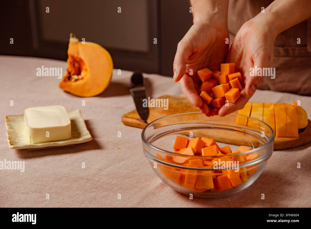 Koch gibt gewürfelten frischen Butternusskürbis in eine Glasschale als Füllung für eine Herbstgalette Stockfoto