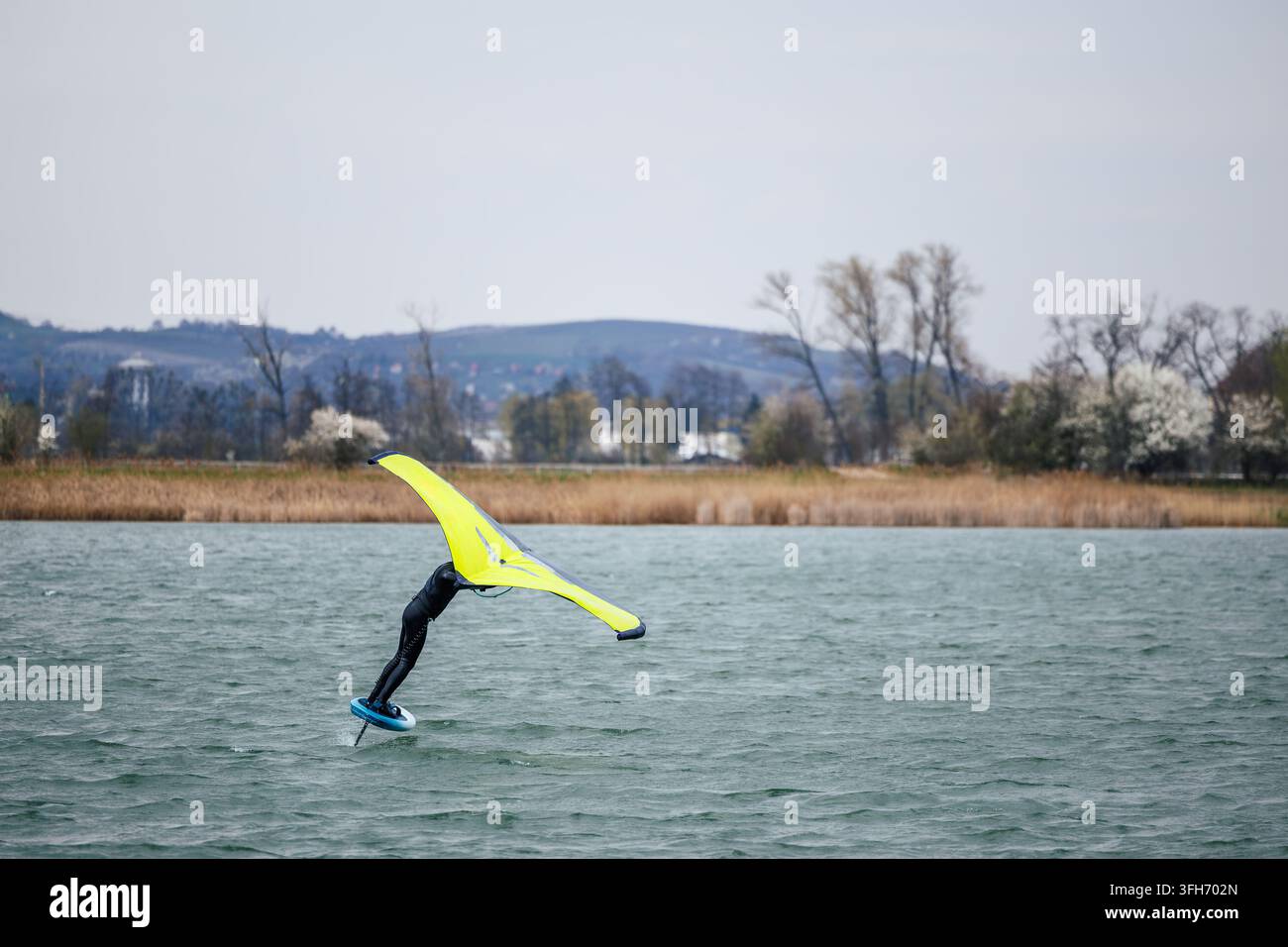 Aquatischer Sport Wingfoiling auf windigem See. Wingfoiler balanciert auf Hydrofoil-Board mit aufblasbarem Flügel Stockfoto