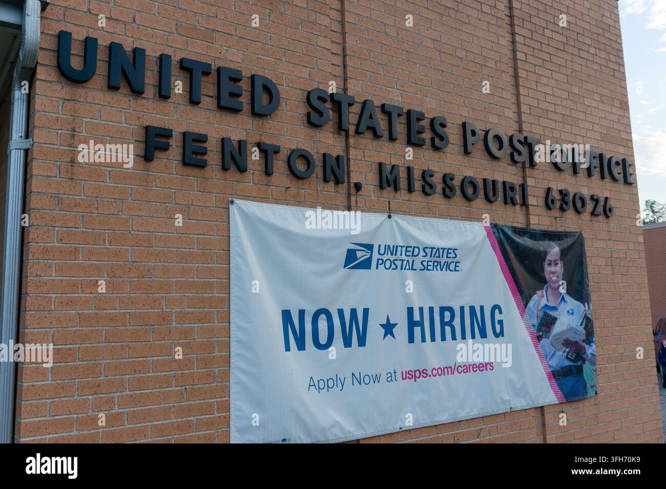 Backstein-Postgebäude in Fenton, Missouri mit Postdienst-Schildern und einem "Jetzt einstellen"-Banner, das lokale Arbeitsplätze und öffentliche Dienstleistungen zeigt. Stockfoto