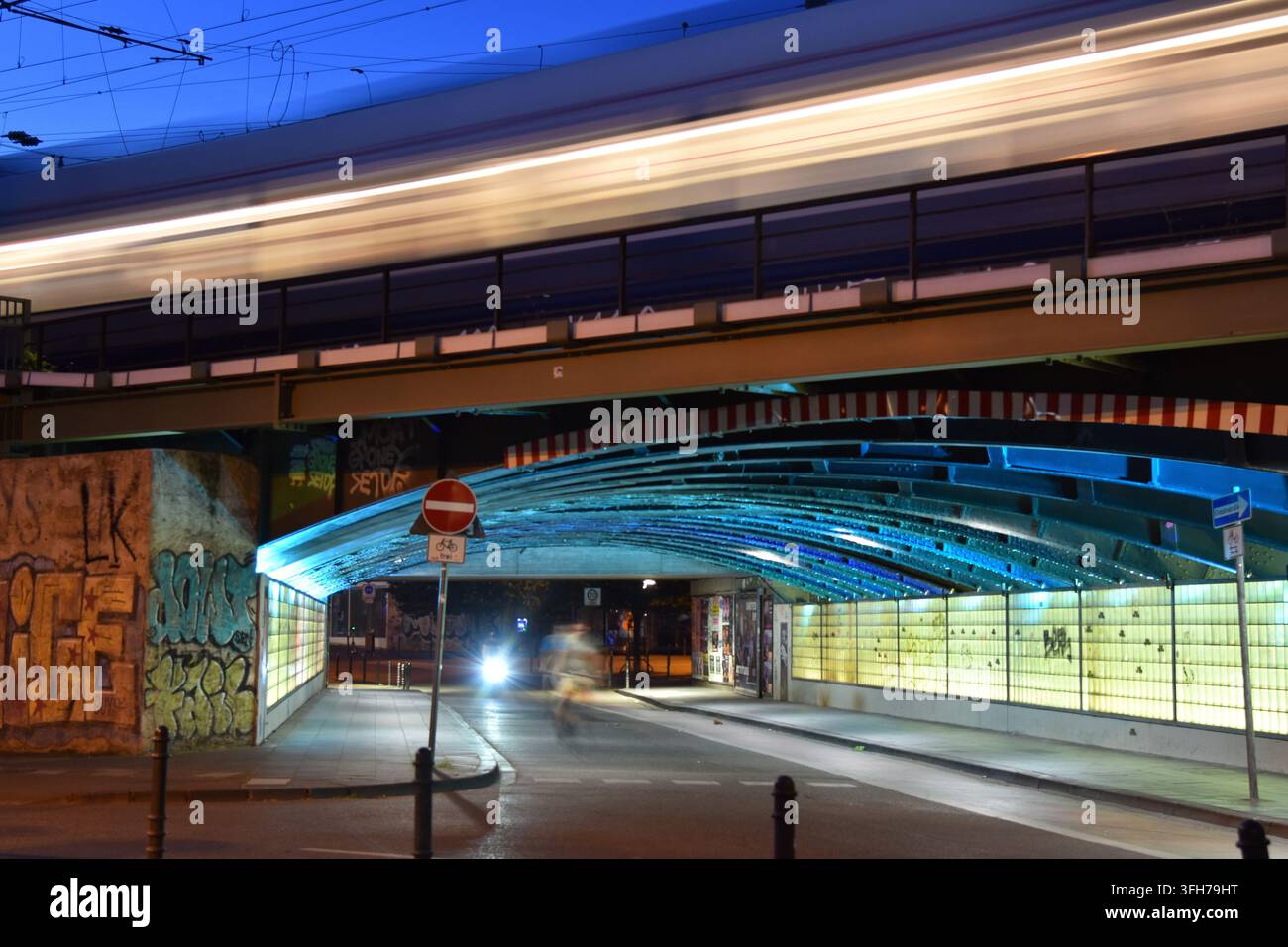 Geisterbild eines Radfahrers, der die beleuchtete Marzellenstraße passiert, während ein Zug die Eisenbahnbrücke darüber überquert, in Köln, Deutschland. Stockfoto