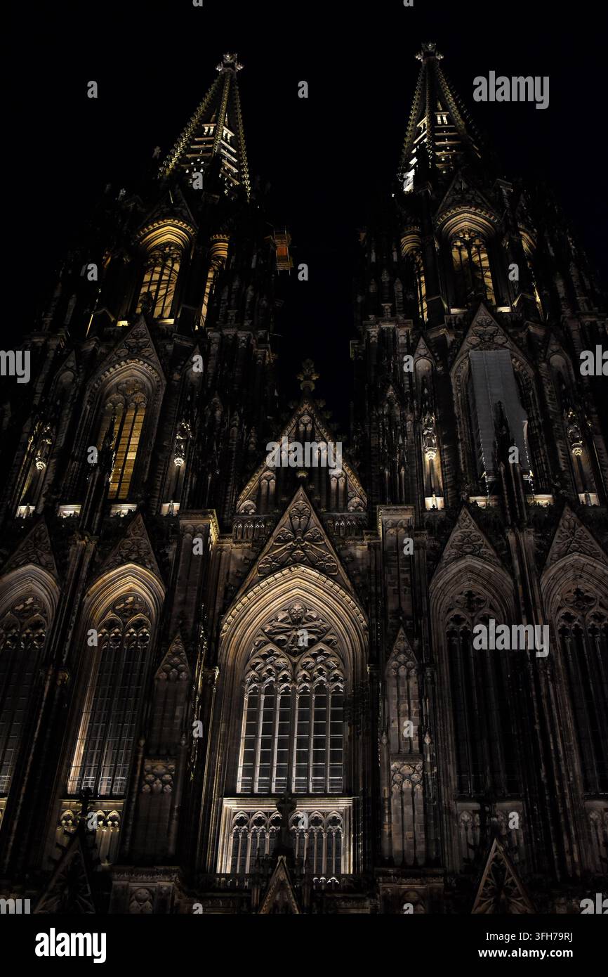 Die Fassade und die beiden gotischen Türme des Kölner Doms bei Nacht, beleuchtet durch Auflicht, vor einem dunklen Himmel. Stockfoto