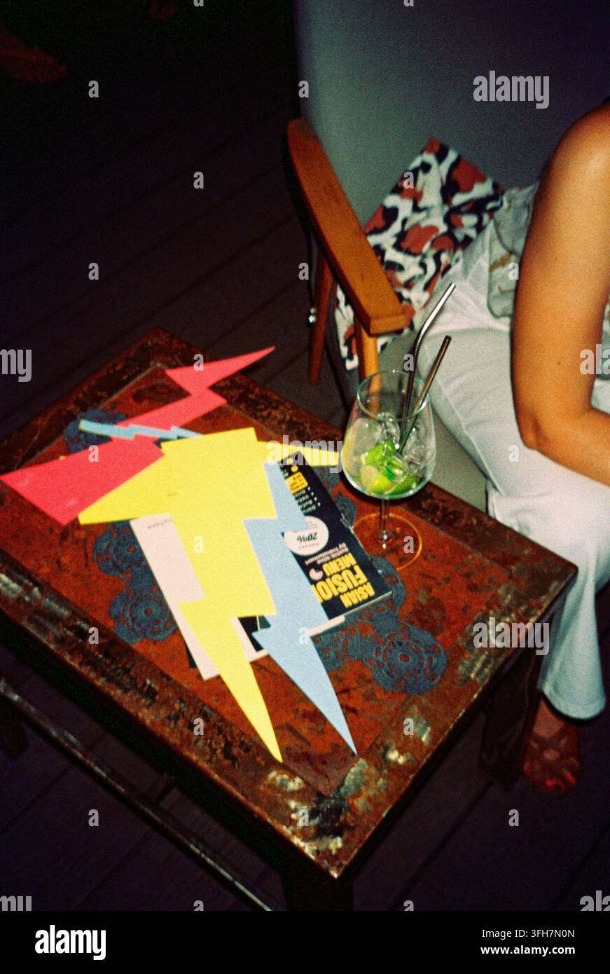 Blitz- und Stromsymbole auf Café-Tischen neben Cocktails, fotografiert mit analogem Blitz für eine mutige Nachtclub-Atmosphäre. Stockfoto