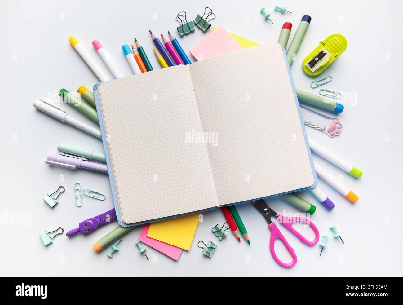 Schulmaterialien um ein offenes Notizbuch auf weißem Hintergrund angeordnet, symbolisieren Bildung und Studium Stockfoto
