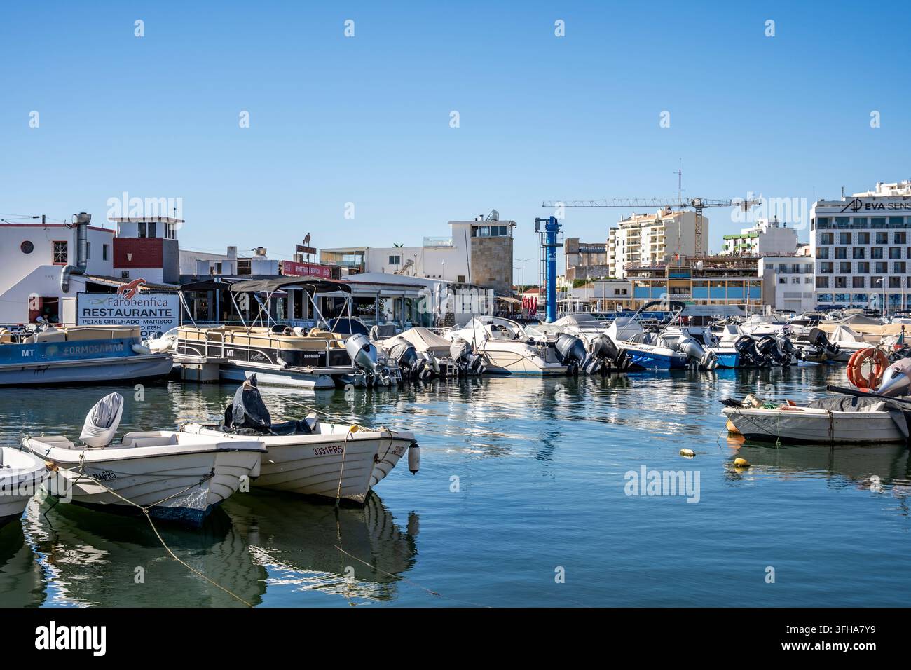Kleine Boote, die in der Faro Marina festgemacht sind, mit dem Ufer und dem historischen Stadtzentrum im Hintergrund, Faro, Algarve, Portugal Stockfoto