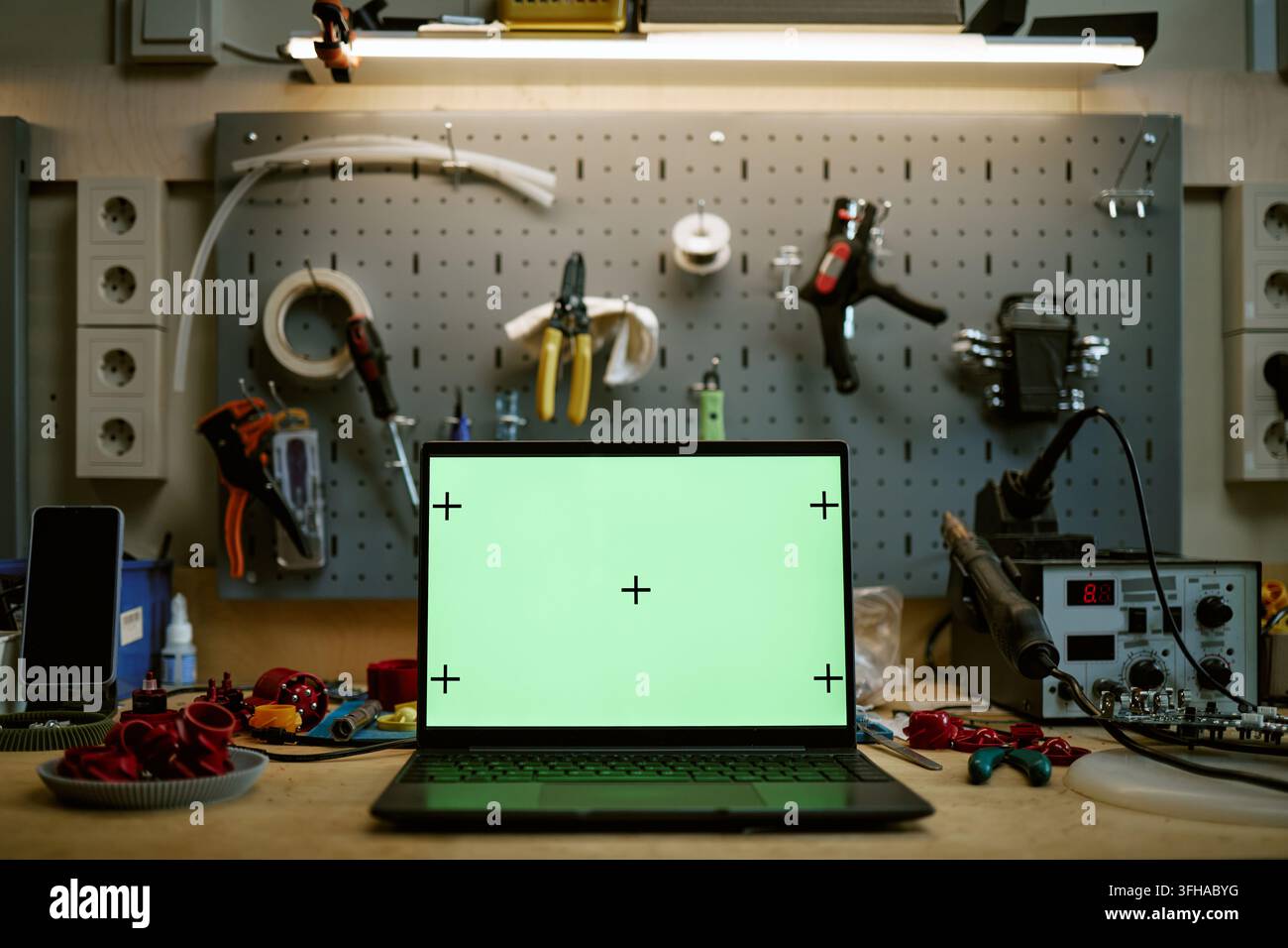 Laptop mit grünem Bildschirm-Mockup auf einem Elektronik-Workshoptisch Stockfoto